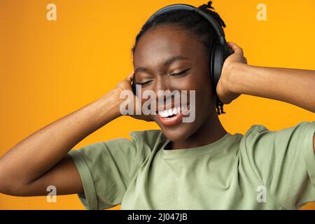 Felice giovane afroamericana donna che ascolta musica in cuffie su sfondo giallo Foto Stock