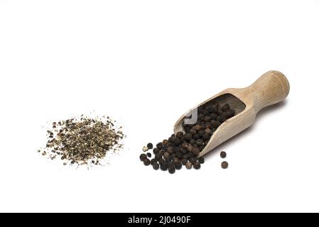 Primo piano di pepe intero e macinato e pepe su pala di legno su sfondo bianco Foto Stock