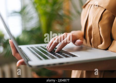 Closeup croppato di inriconoscibile imprenditore floreale negozio in piedi con laptop tenuta in mano tra piante verdi. Foto Stock