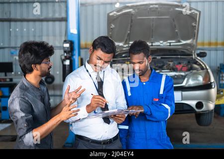 Cliente che discute con il meccanico e il responsabile del garage dei problemi dell'auto durante il servizio di riparazione o manutenzione - concetto di comunicazione con il cliente e. Foto Stock