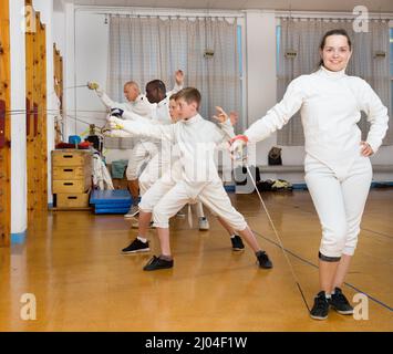 Giovani femmine fencer in piedi con la griffa alla palestra sullo sfondo con gruppo impegnato nella scherma Foto Stock