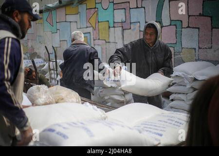 I venditori palestinesi caricano sacchi di farina su un carro trainato da cavalli di fronte al centro di distribuzione degli aiuti alimentari dell'UNRWA ad ovest di Gaza. La scarsità dei prodotti alimentari di base ha causato un aumento dei prezzi nella striscia di Gaza. La regione è fortemente dipendente dalle forniture di grano provenienti dall'Ucraina e dalla Russia che sono ora in guerra. Foto Stock