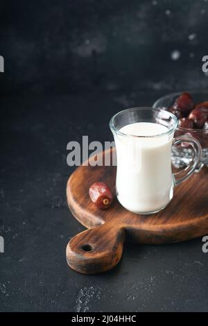 Ramadan Kareem cibo e bevande. Piatto di datteri, bicchiere di latte e ramo di palma di datteri su sfondo nero. Stile di vita musulmano giusto. Cibo vegetariano. S Foto Stock