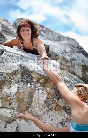 Dare una mano. Una donna che aiuta il suo compagno di arrampicata su una scogliera. Foto Stock