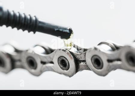 Lubrificare una catena di bicicletta con una goccia di olio da vicino su uno sfondo grigio isolato. Manutenzione del sistema di trasmissione bicicletta Foto Stock