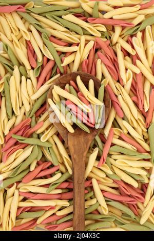 Fusilli pulgiesi pasta tricolore in un cucchiaio di legno d'oliva e formando uno sfondo astratto. Sano concetto di cibo italiano carboidrato. Foto Stock