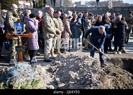 Non esclusiva: LVIV, UCRAINA - 15 MARZO 2022 - Un uomo getta terreno nella tomba durante i funerali militari dei militari della Hetman Petro SA Foto Stock