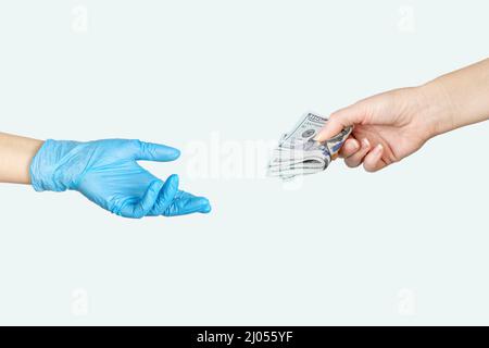 La mano femminile del paziente dà un medico in blu guanti medici soldi cento dollari fatture. Medicina pagata. Costi per l'assicurazione medica Foto Stock