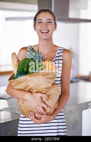 Una vita sana è una vita felice. Una donna attraente che tiene una borsa di generi alimentari in cucina. Foto Stock