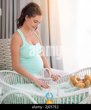 Momenti speciali sulla strada. Shot di una donna incinta in piedi accanto alla sua culla babys nella stanza dei bambini. Foto Stock