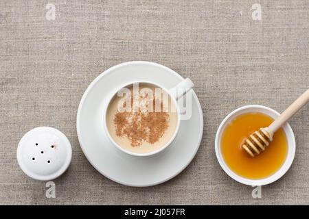 Tè piccante con latte in una tazza di porcellana bianca con cucchiaia di miele e miele su sfondo tessile Foto Stock