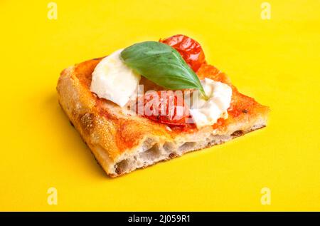 Un pezzo di pizza al taglio con pomodoro e mozzarella isolato su sfondo giallo Foto Stock