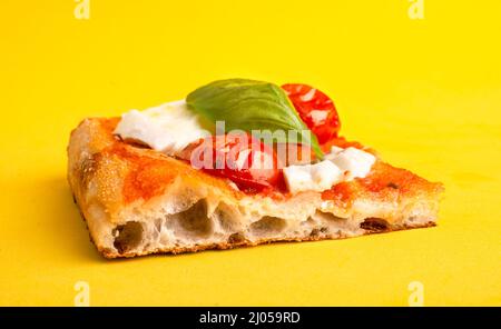 Un pezzo di pizza al taglio con pomodoro e mozzarella isolato su sfondo giallo Foto Stock