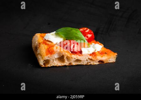 Un pezzo di pizza al taglio con pomodoro e mozzarella isolato su sfondo nero Foto Stock