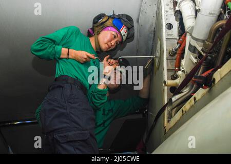 Guam. 7th Mar 2022. Aviation Machinist's Mate 2nd Class Michelle Berry, davanti, da Prince George, Va., E Aviation Machinist's Mate 3rd Class Corey Gust, di Littleton, Colom., eseguire la manutenzione su un e-2D Hawkeye, assegnato ai 'Wallbangers' della Carrier Airborne Early Warning Squadron (VAW) 117, nella baia di hangar a bordo del vettore aereo di classe Nimitz USS Abraham Lincoln (CVN 72). Abraham Lincoln Strike Group è in fase di implementazione programmata nell'area delle operazioni della flotta USA 7th per migliorare l'interoperabilità attraverso alleanze e partnership, fungendo da forza di risposta pronta i Foto Stock