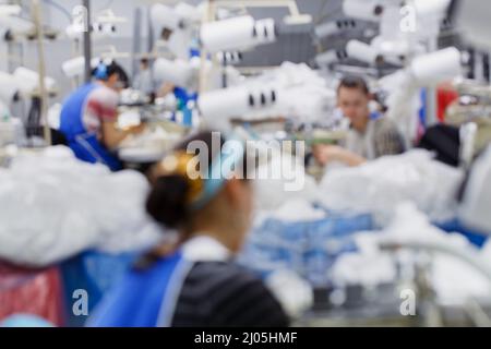 Sfocare lo sfondo con le donne sono impegnati nella sartoria di collant in una fabbrica Foto Stock