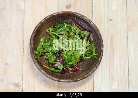 Insalata di foglie verdi (rucola, barbabietola, spinaci) su una rustica ciotola di legno intagliata Foto Stock
