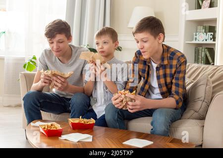 Un felice tre ragazzi adolescenti, mangiando fast food in soggiorno Foto Stock