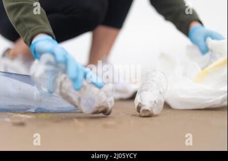 Primo piano. Le mani di un volontario in guanti puliscono i rifiuti, bottiglie di plastica usate sulla spiaggia. Problemi ambientali globali, inquinamento ambientale, Foto Stock