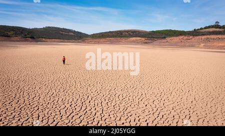 Silhouette di un uomo su una terra sabbiosa spaccata vuota e non fertile durante una siccità. Il concetto di catastrofe ecologica sul pianeta. Foto Stock