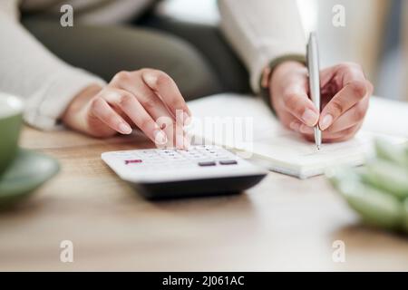 Fare alcuni calcoli per garantire che le risorse finanziarie siano sulla buona strada. Primo piano di un'irriconoscibile donna d'affari che scrive note mentre usando una calcolatrice Foto Stock