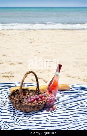 Picnic sulla spiaggia con vino rosato, pane francese baguette e uva Foto Stock