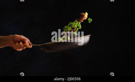 Uno chef professionista cuoce il polpo con verdure, erbe e fette di limone in una padella. Levitazione. Sfondo nero. Cucina orientale, frutti di mare rec Foto Stock