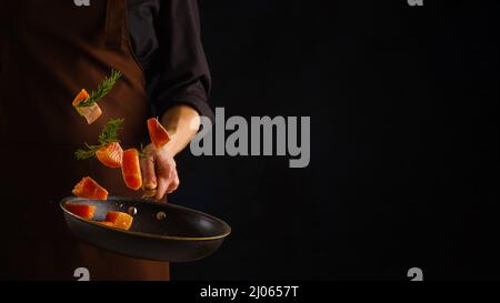 Uno chef professionista prepara frutti di mare - pezzi di trota rossa, salmone con verdure in una padella su sfondo nero. Levitazione. Cucina di mare, healt Foto Stock