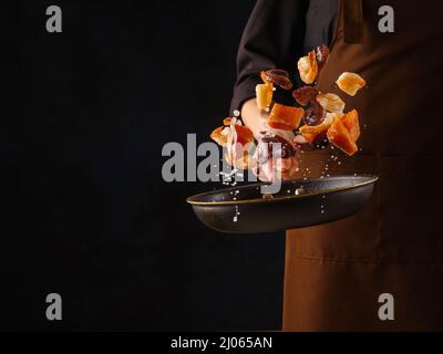 Frutti di mare. Uno chef professionista prepara pezzi di pesce rosso - salmone, trota e polpo in una padella su sfondo nero. Cibo congelato a bordo. Se Foto Stock