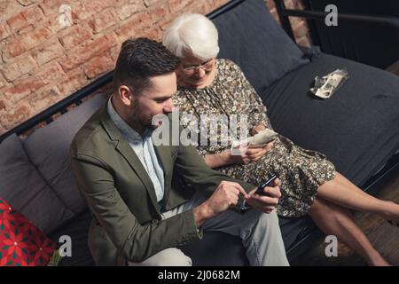 due persone di una famiglia seduti sul divano e guardando fotografie digitali e stampate. Foto di alta qualità Foto Stock