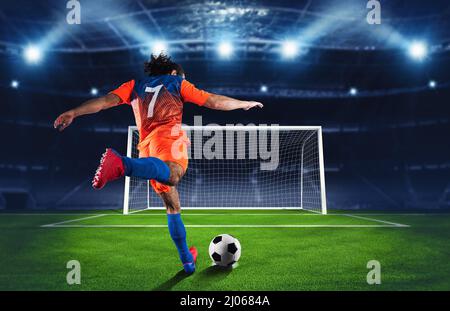 Scena di calcio di notte partita con giocatore in una uniforme arancione e blu calci il calcio di punizione Foto Stock