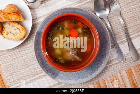 Abbondante zuppa fatta in casa con carne di maiale su osso e verdure servite con verdure verdi. Foto Stock