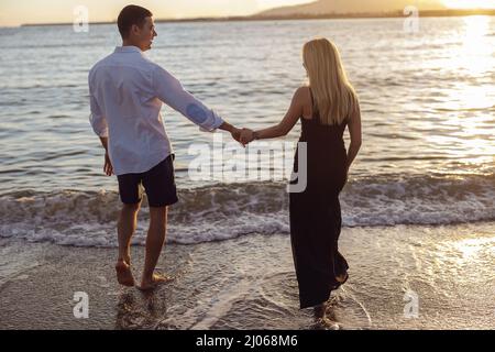 Vista posteriore di una bella coppia che cammina verso il mare al tramonto Foto Stock