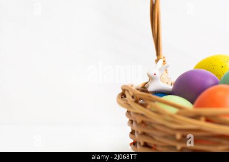 Uova di Pasqua colorate in cestino di vimini con coniglietto in ceramica. Felice Pasqua concetto Foto Stock
