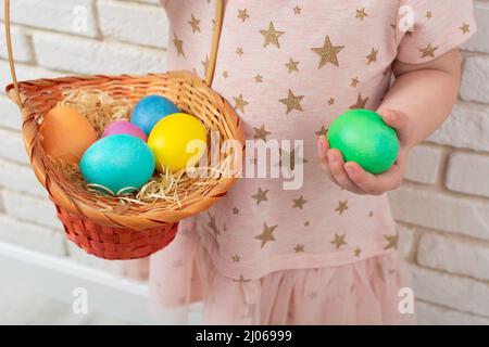 Ragazza irriconoscibile con uova di Pasqua colorate in cestino di vimini. Primo piano Foto Stock