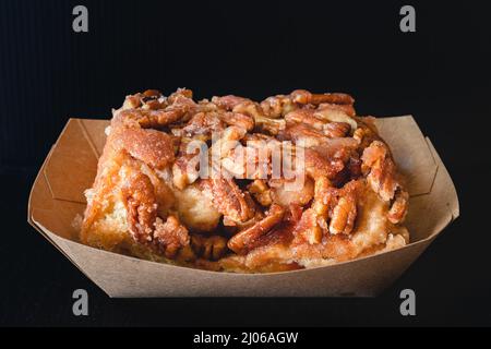 Rotolo di cannella ghiacciato Pecan da vicino su sfondo nero Foto Stock