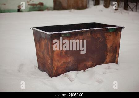 Il contenitore arrugginito si trova nella neve. La spazzatura può fuori. Spazzatura in Russia. Vecchia tanica di raccolta rifiuti. Foto Stock