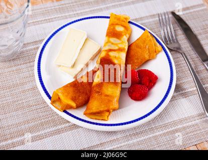 Pancake sottili e delicati con fette brie, lamponi freschi e maturi e miele. Deliziosa colazione fatta in casa. Foto Stock