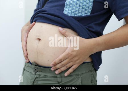 Vista di un maschio adulto che tiene il suo ventre grande con la sua camicia in su Foto Stock