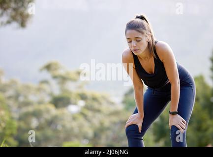 Alcuni giorni saranno più impegnativi di altri. Scatto di una giovane donna sportiva che cattura il respiro mentre si esercita all'aperto. Foto Stock