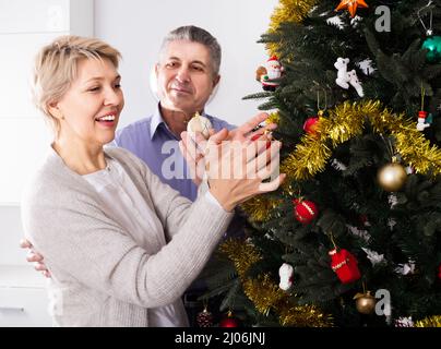 Donna e uomo 50-55 anni sono riagganciare Nuovo Anno di giocattoli su un abete bianco prima di Natale. Foto Stock
