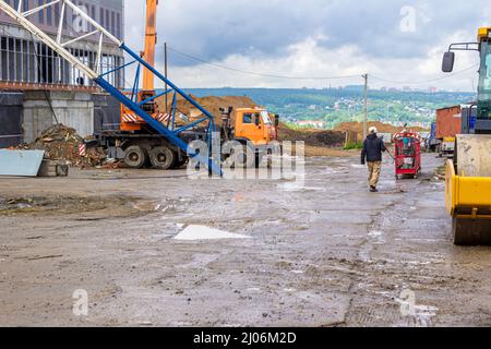 un cantiere con una strada temporanea fiancheggiata da lastre di cemento, su cui è presente una gru per camion e attrezzature stradali, in cumuli di argilla a distanza Foto Stock