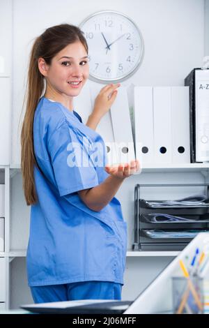 Femmina e giovane assistente medico a lavorare in ufficio in piedi vicino a ripiani con le cartelle Foto Stock