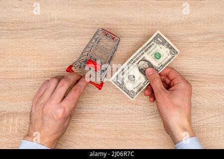 L'uomo d'affari spinge il carrello giocattolo e tiene una fattura del dollaro nella mano. Concetto di shopping Foto Stock