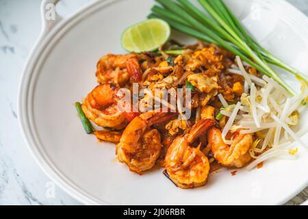 Gamberetti Pad Thai o tradizionale menu di noodle Thai, Pad Thai in elegante piatto bianco di forma rotonda su tavolo di marmo, immagine ravvicinata cibo tailandese. Foto Stock