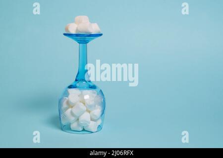 Marshmallows bianchi in un bicchiere da vino rovesciato su sfondo blu Foto Stock