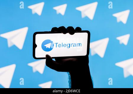 Smartphone con messaggio telegramma sullo schermo in una mano applaiata sullo sfondo dei logo telegramma Foto Stock