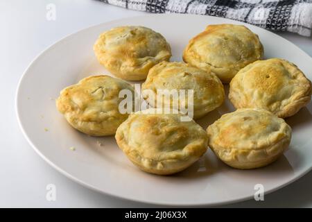 Mini torte alla bistecca su un piatto - piccole torte salate al forno da vicino su sfondo bianco Foto Stock