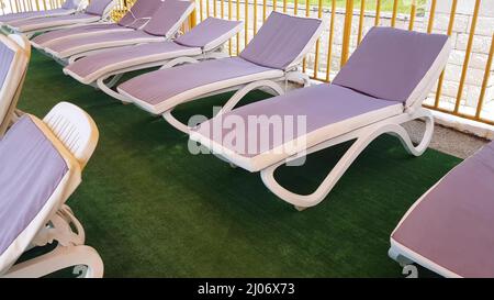 sedie a sdraio vuote si trovano in fila sotto il tetto del solarium per prendere i bagni d'aria sulla riva del mare, una località turistica Foto Stock