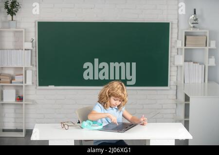 Bambino della scuola che usa il portatile digitale del pc in classe. Ritratto di divertente allievo della programmazione dello studio della scuola primaria. Foto Stock